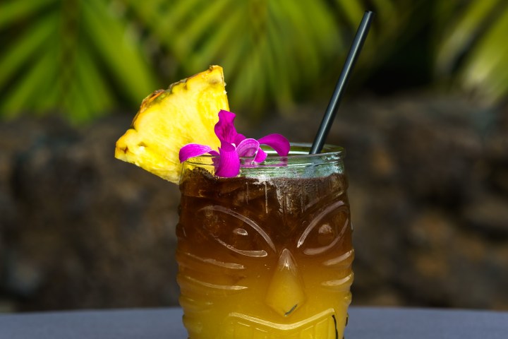 Tiki cocktail with pineapple slice and orchid garnish, black straw.