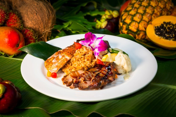 Plate with grilled chicken, rice, vegetables, and flower garnish, surrounded by tropical fruits.