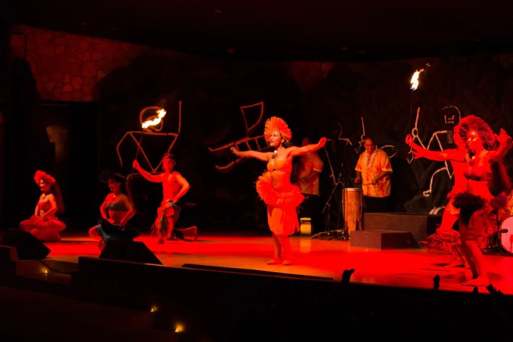 Performers in traditional costumes dance on stage with torches in an outdoor venue.